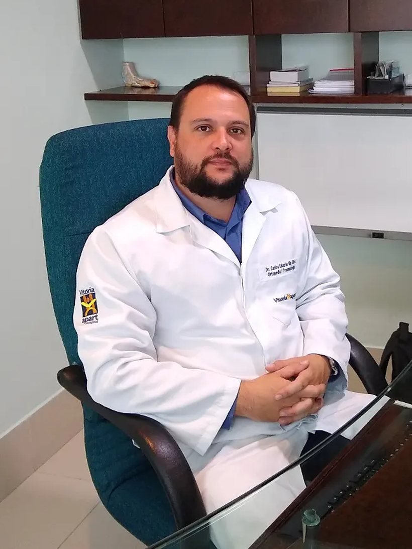 Dr. Carlos Eduardo Sily de jaleco branco, sentado em seu consultório